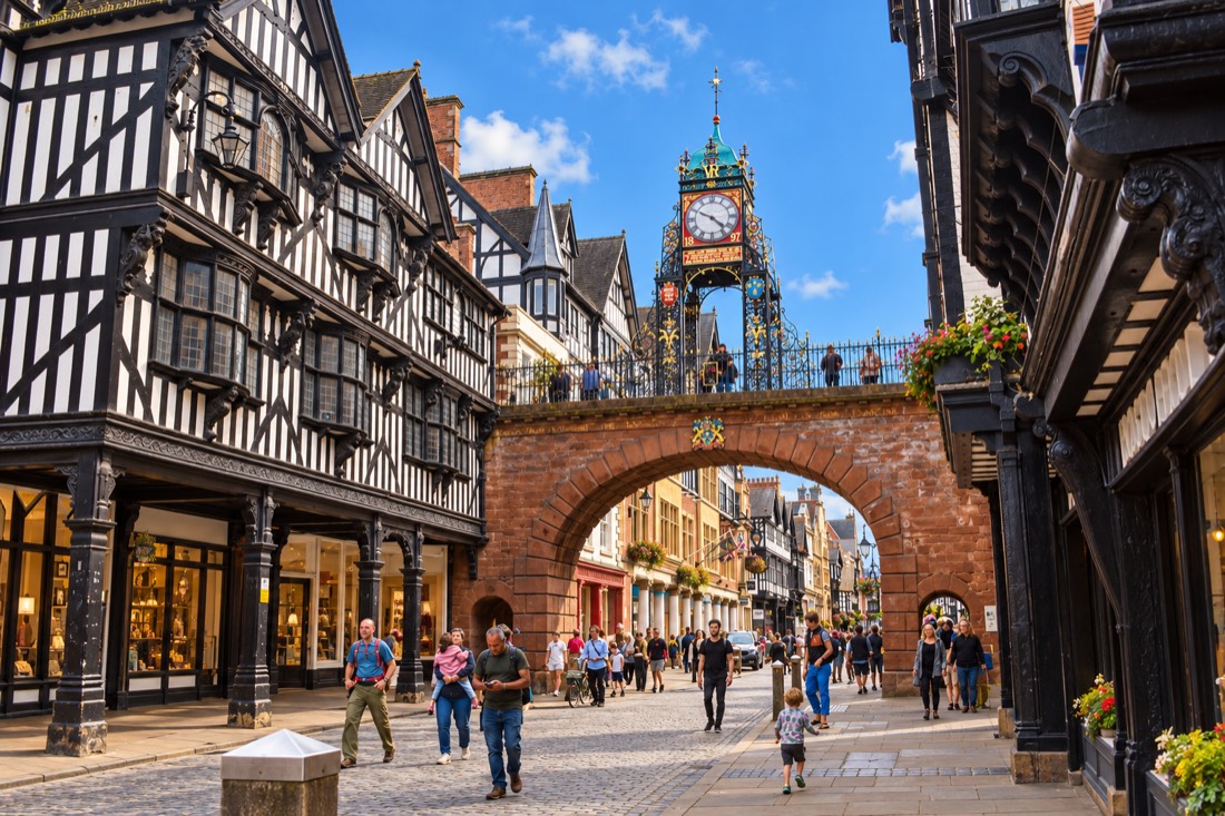 The Eastgate Clock arching over a busy street of black and white timber buildings in Chester